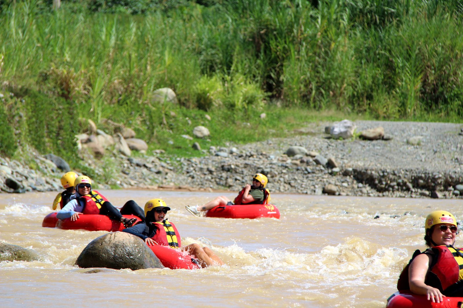 A group of guests in tubes floats past a big river rock