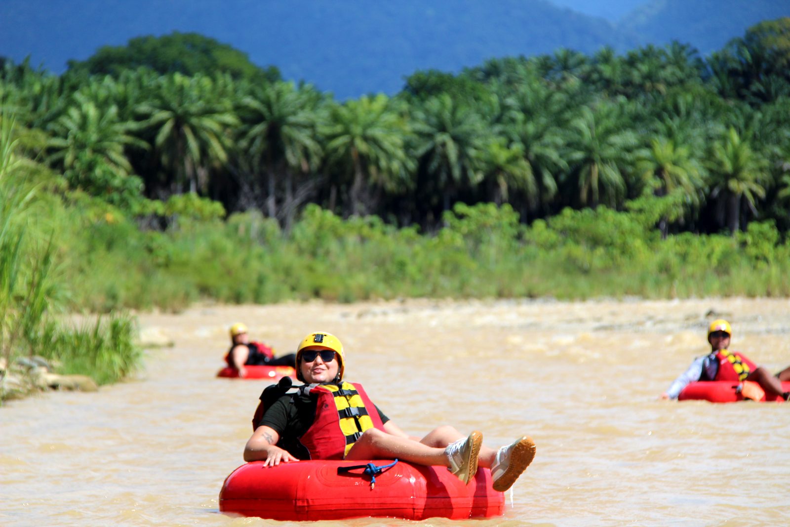 A smiling guest in her tube, with oil palms on the bank