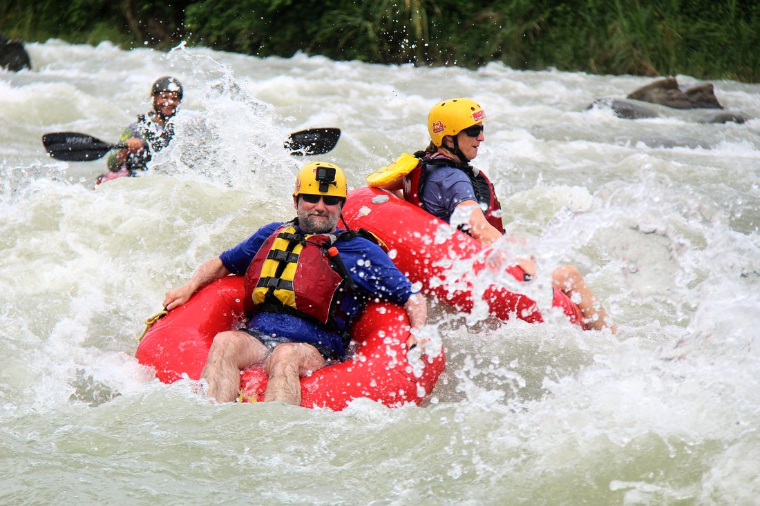 Two tubers splashing through a rapid with the safety kayaker behind